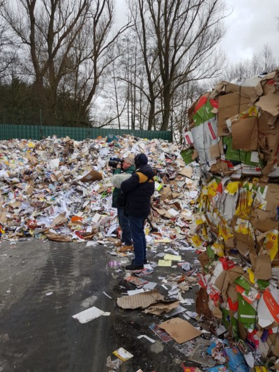 Kamerateam steht vor Berg aus Papiermüll