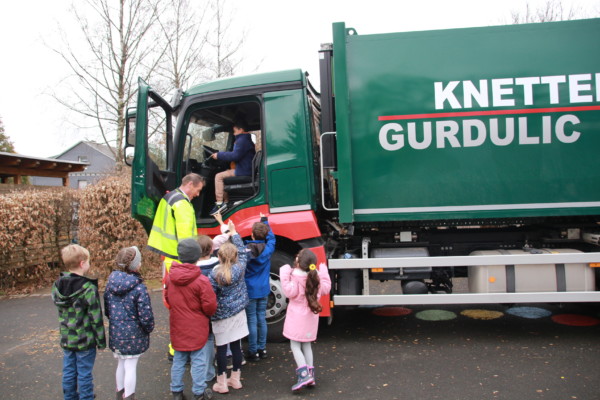 Kinder stehen vor dem Abfuhrfahrzeug, um sich ans Steuer setzen zu dürfen.