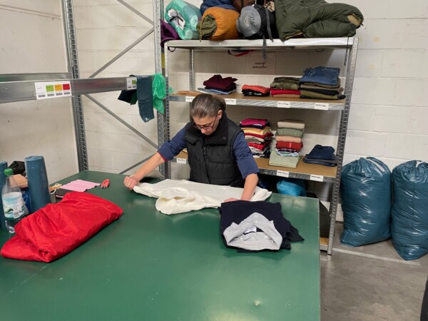Eine Frau steht an einem Tisch und begutachtet den darauf liegenden Pullover.